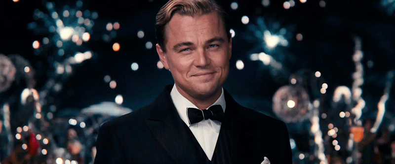 Leonardo DiCaprio's character in The Great Gatsby raising a glass and cheering.
